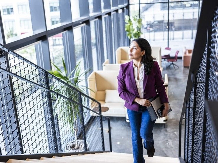 An adult professional walking up the stairs in an office setting. 