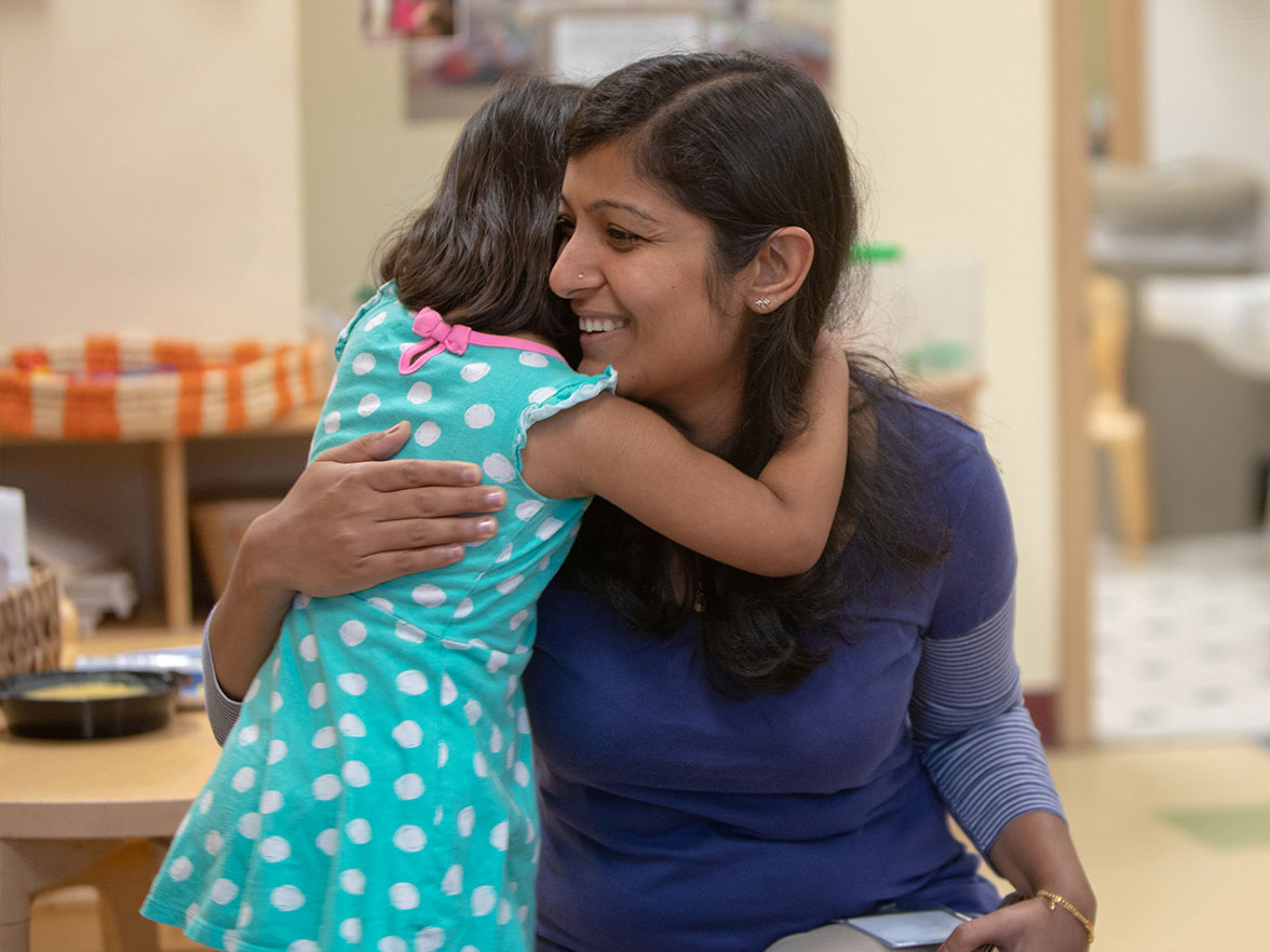Young woman hugs child in blue dress | Bright Horizons