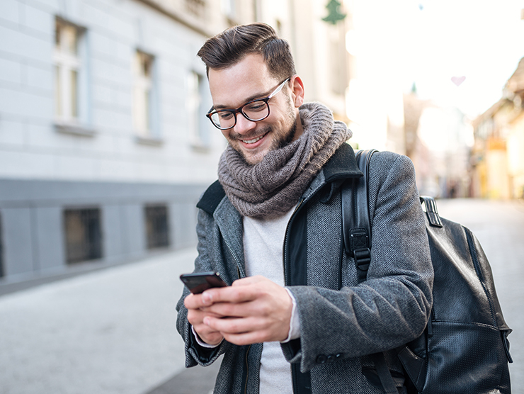 young male smiling looking at smartphone on street