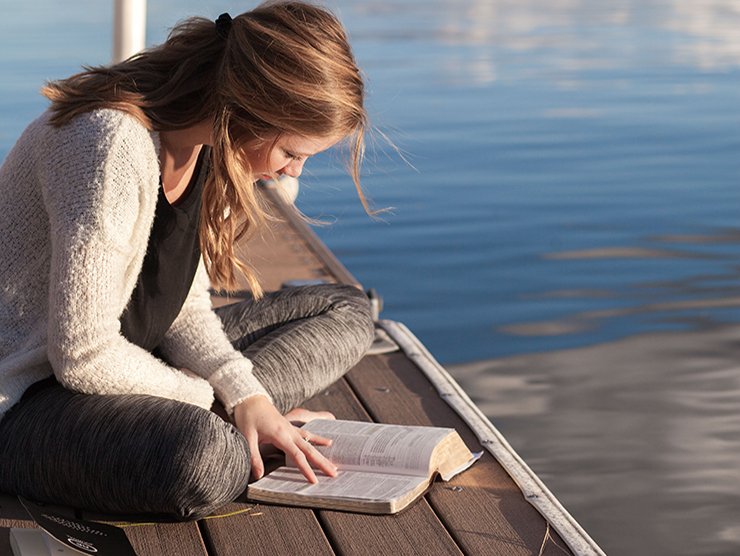 Young female adult learner studying on a dock during summer