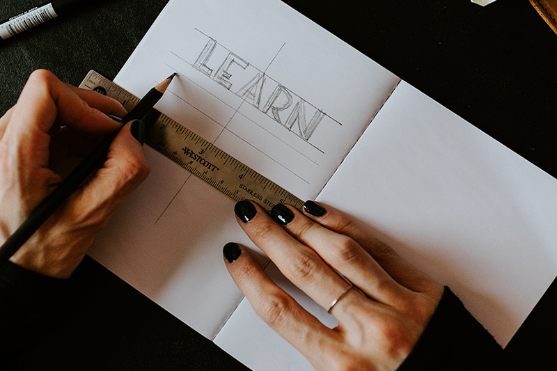 Hands writing "Learn" in block letters in a notebook