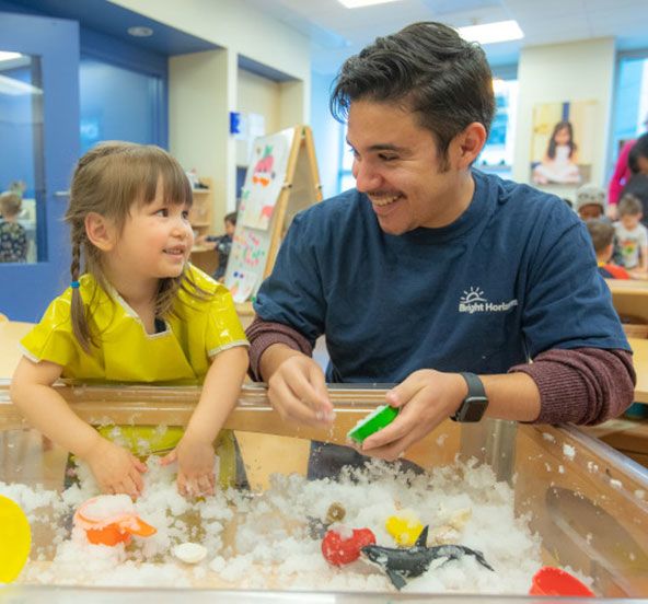 A child care teacher helps a young learner at daycare