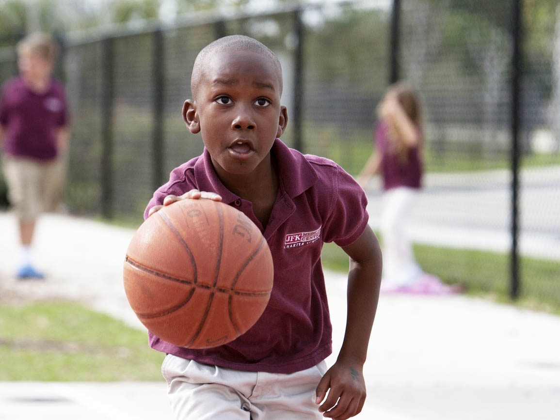 Elementary school-aged boy playing baseketball outside