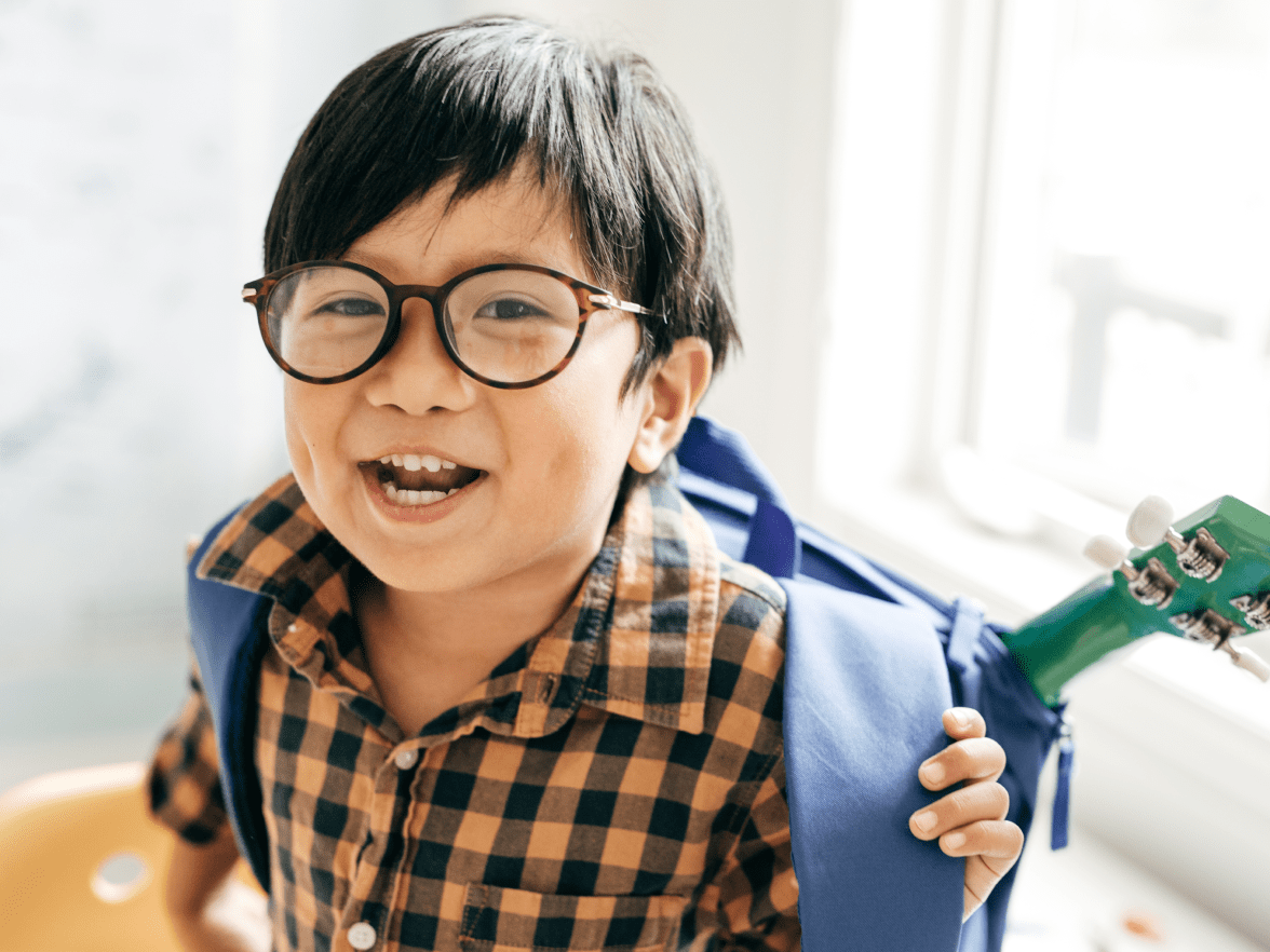 Child with glasses smiling and putting on backpack