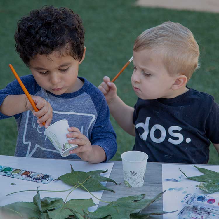 Two toddler boys painting together outside