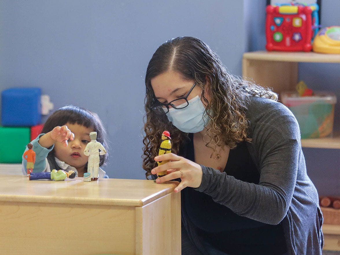 Daycare teacher wearing a mask to be safe while playing with a child at Bright Horizons