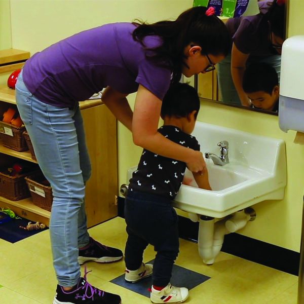 Teacher helping toddler wash hands