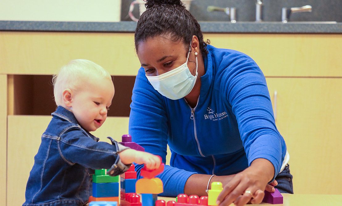 Teacher in mask at daycare with young toddler | Bright Horizons health and safety