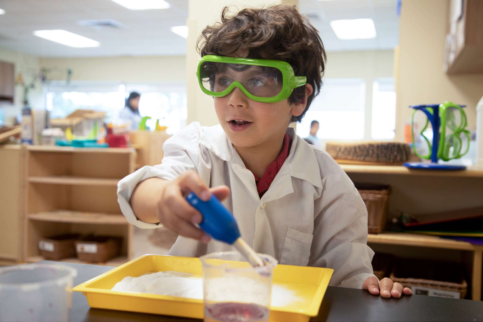 A young boy in a lab coat and safety goggles conducts a science experiment at daycare | Bright Horizons