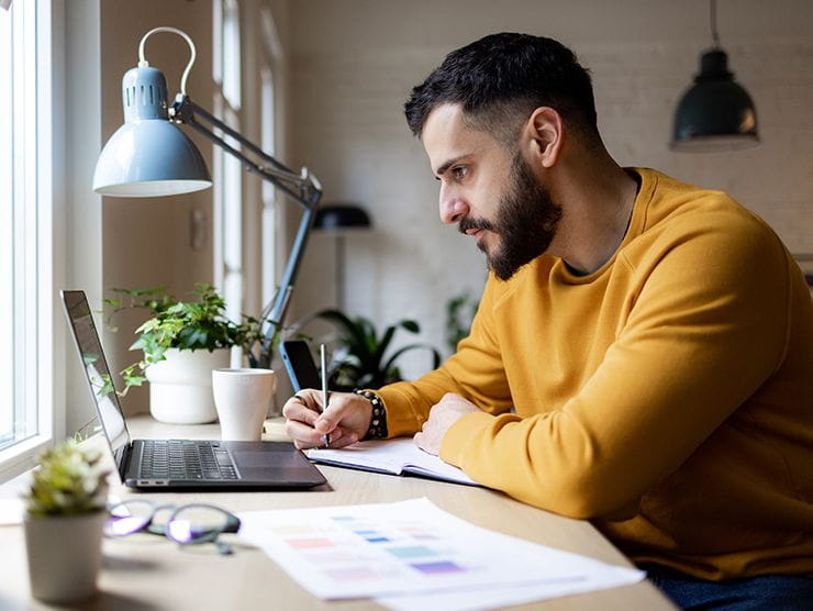 Adult male sitting at his desk by the window, looking at his laptop
