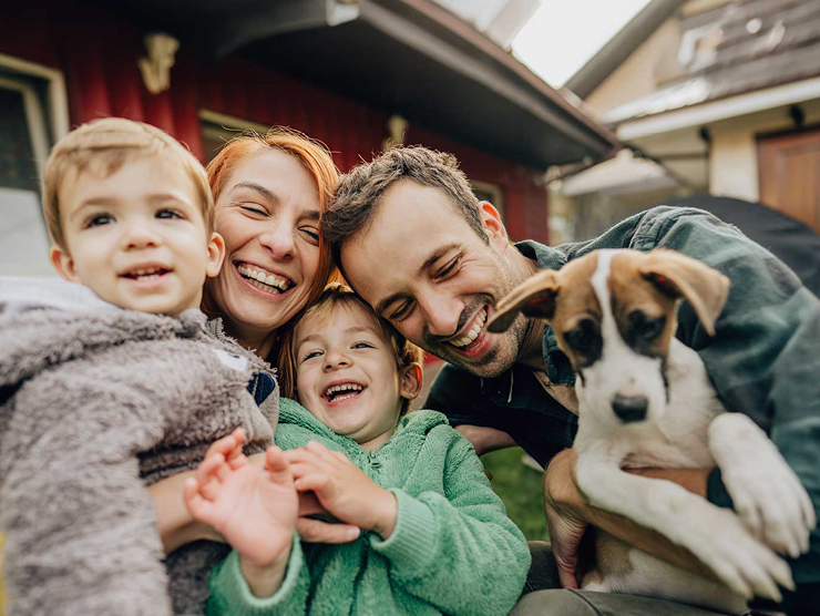 A family with 2 young children and a dog smiling 