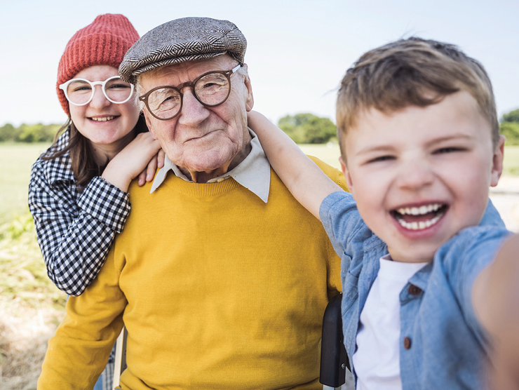 A young child, elderly man, and middle aged woman smiling at the camera for a picture