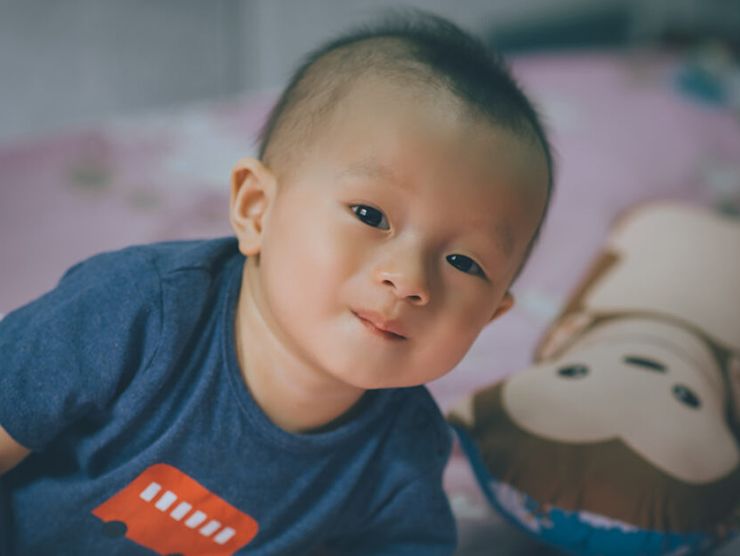 Toddler crawling on mat next to a stuffed animal at home 
