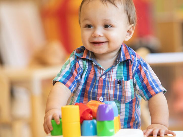 Toddler building with colored plastic blocks and smiling at Bright Horizons day care 