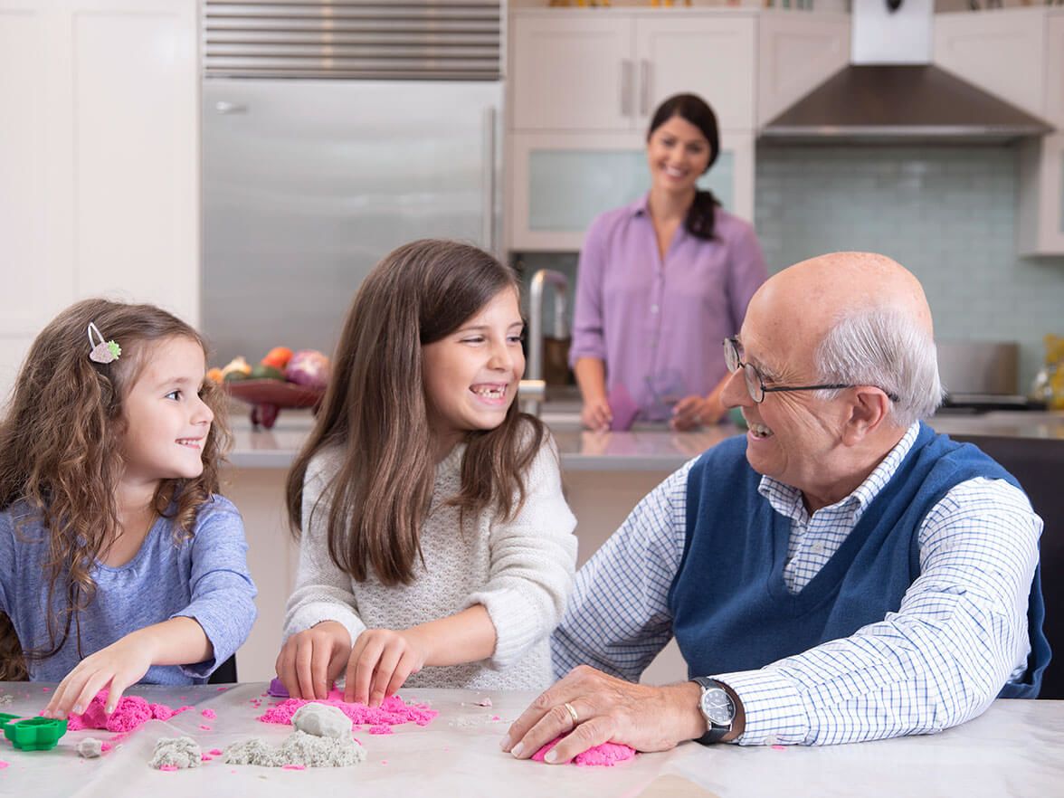 Caregiver watching on as grandfather interacts with granddaughters 