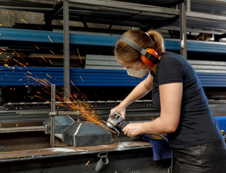 Woman using power tool to saw metal piece