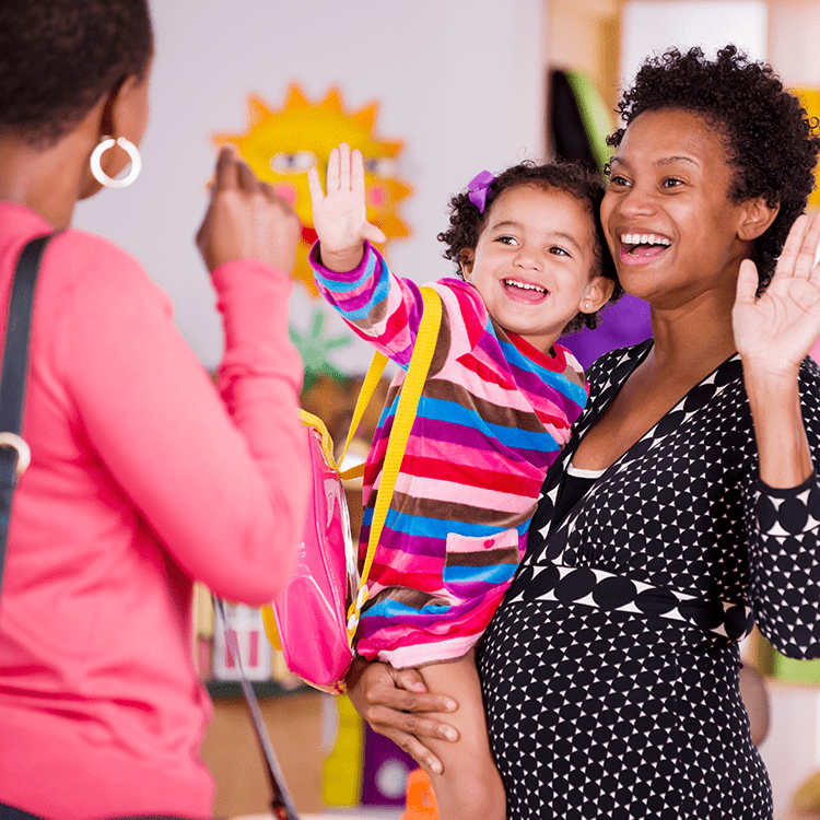 Caregiver holding child waving goodbye to parent smiling