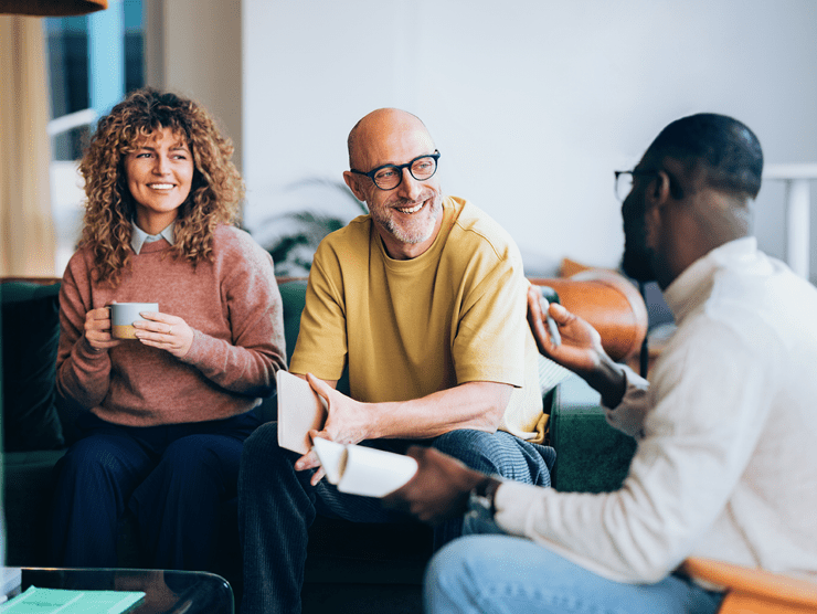 Three adult professionals talking to each other while sitting  on a couch. 