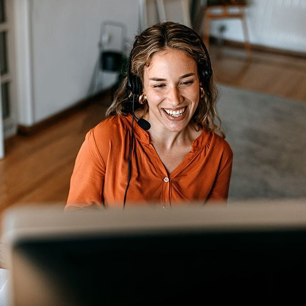 Woman wearing a headset, sitting at home, smiling at her computer