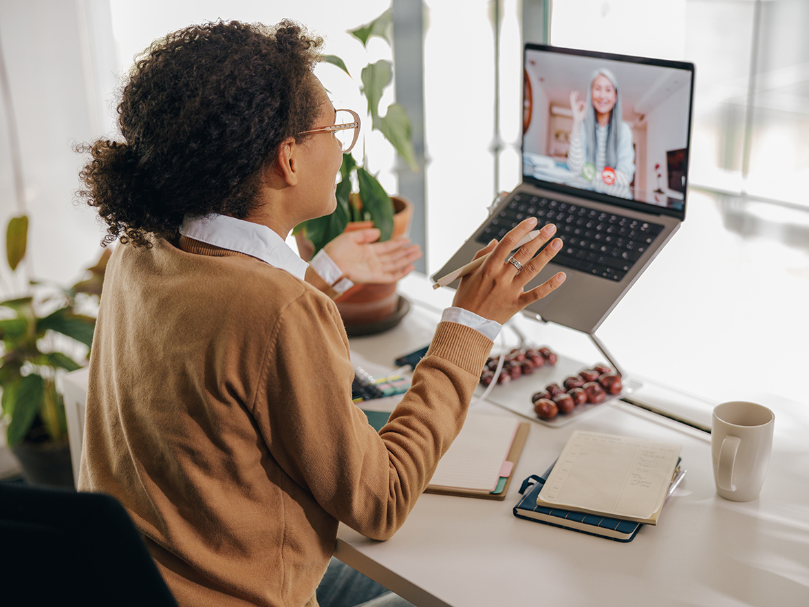 Woman sitting at a desk with her laptop on a stand, engaging in a video meeting with another woman