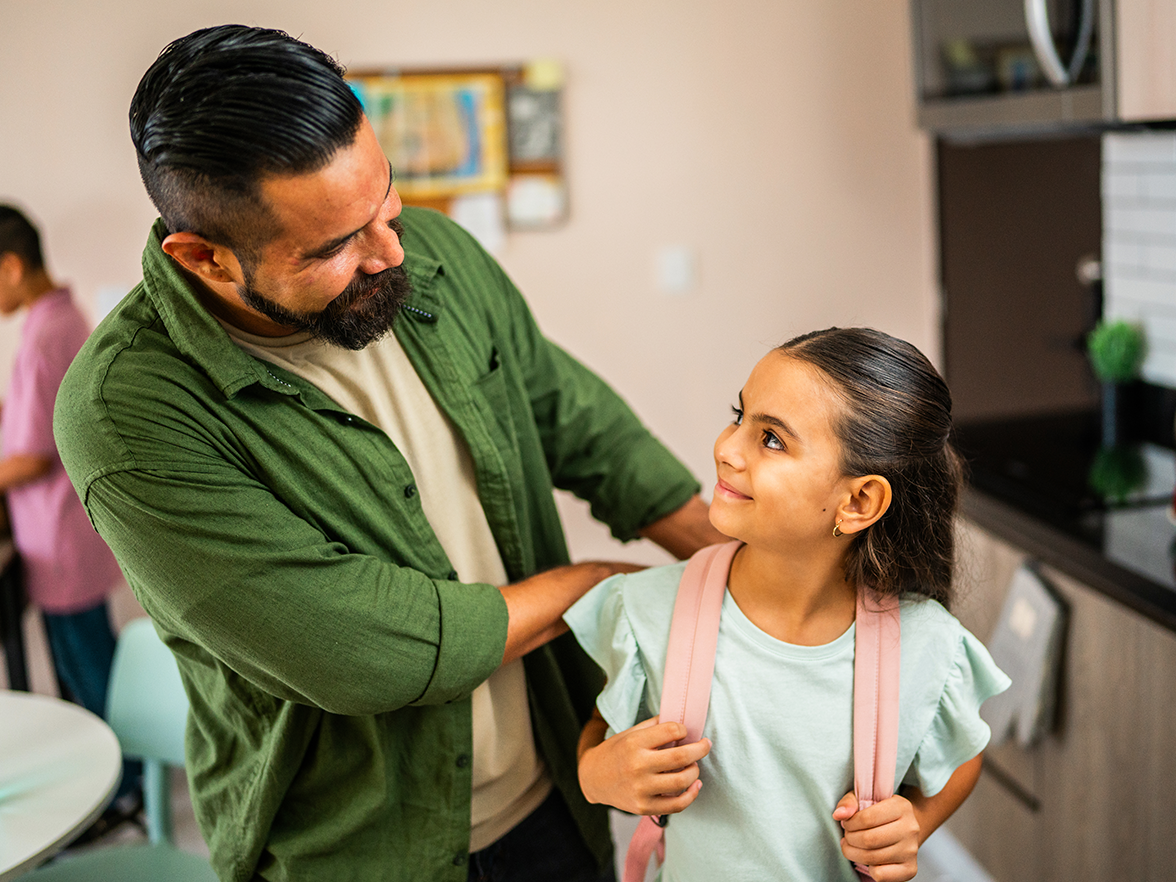 Father helping daughter put on her backpack