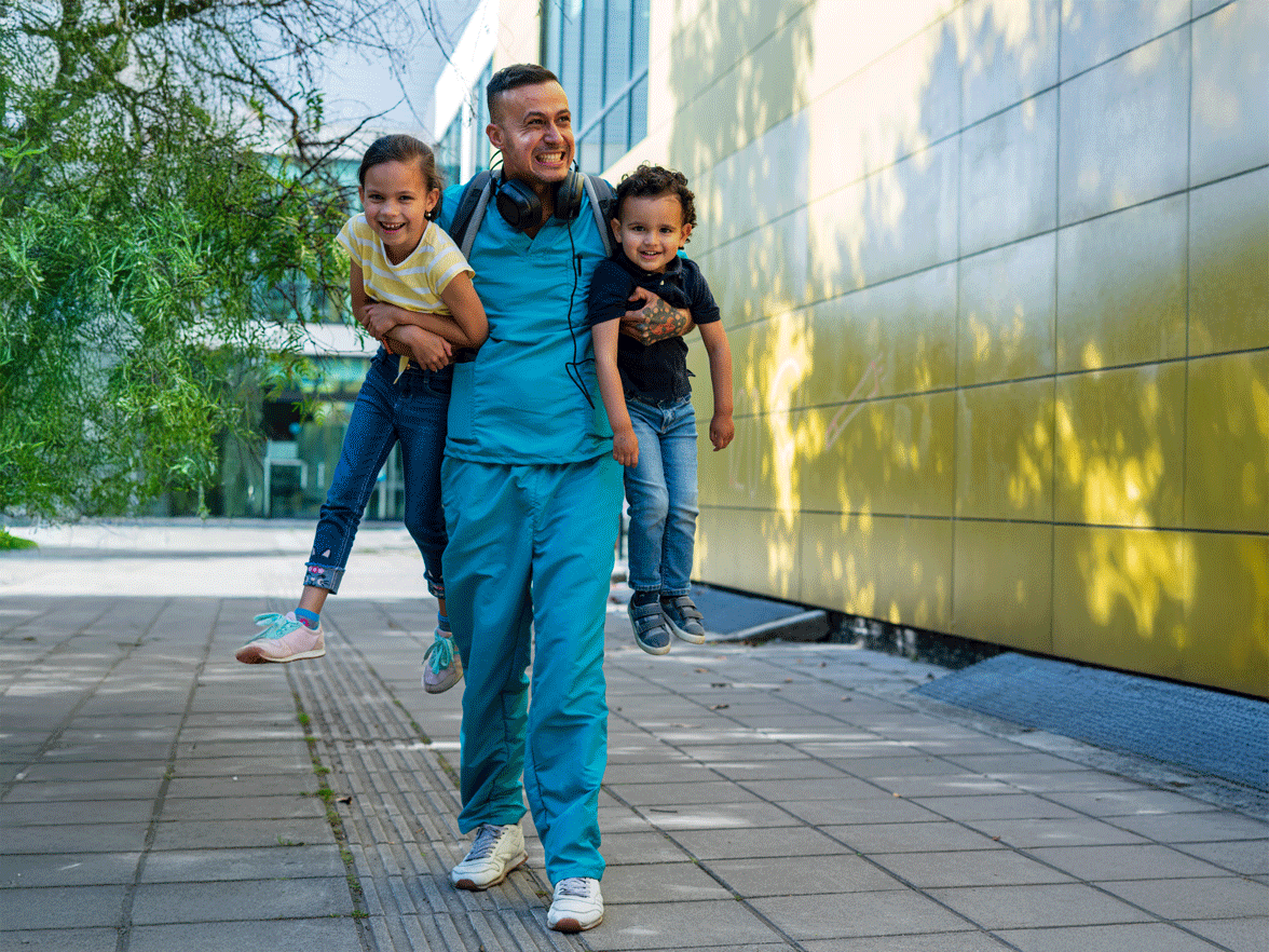 Father in scrubs carrying two children smiling