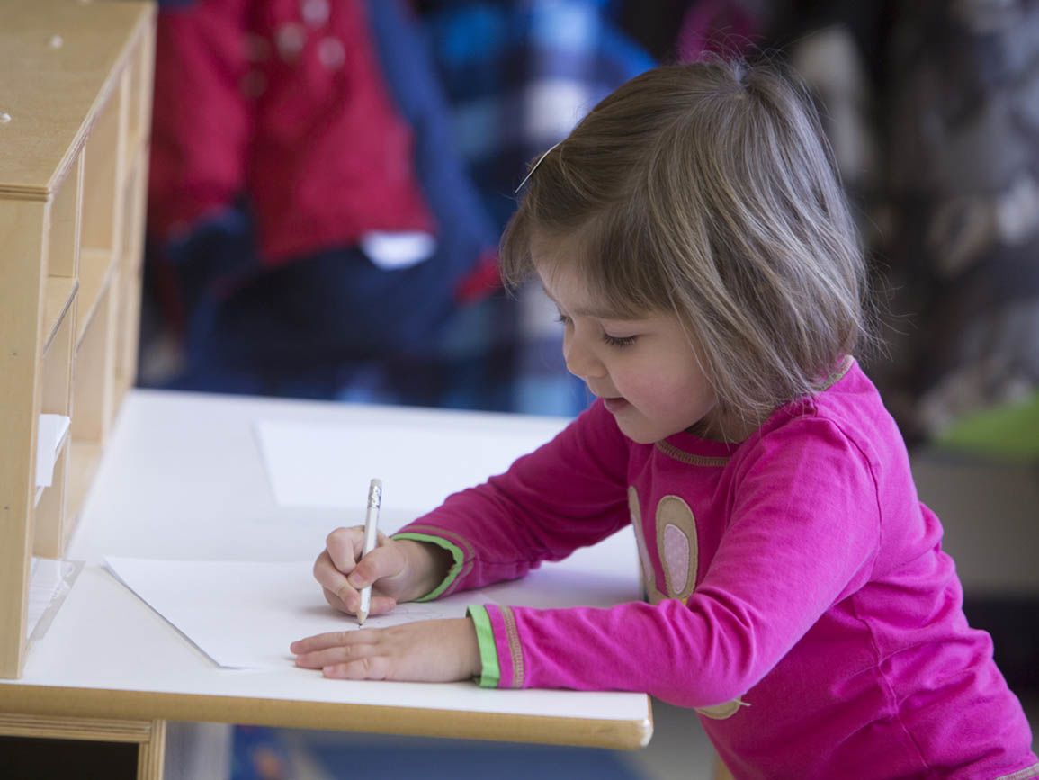A toddler girl writing at her desk