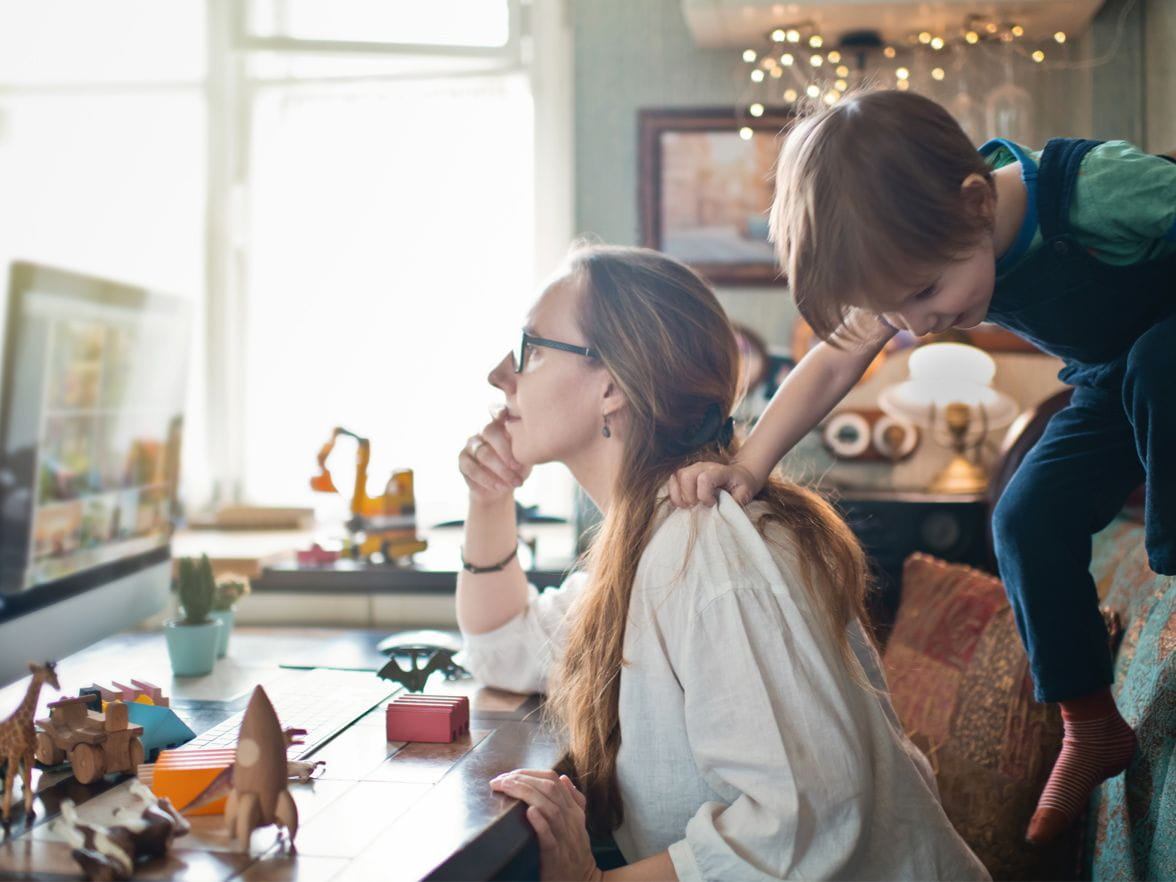 Mother working with child in background crawling over her