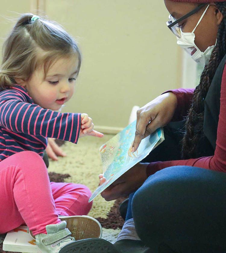 Teacher with transparent mask reads to toddler | Bright Horizons
