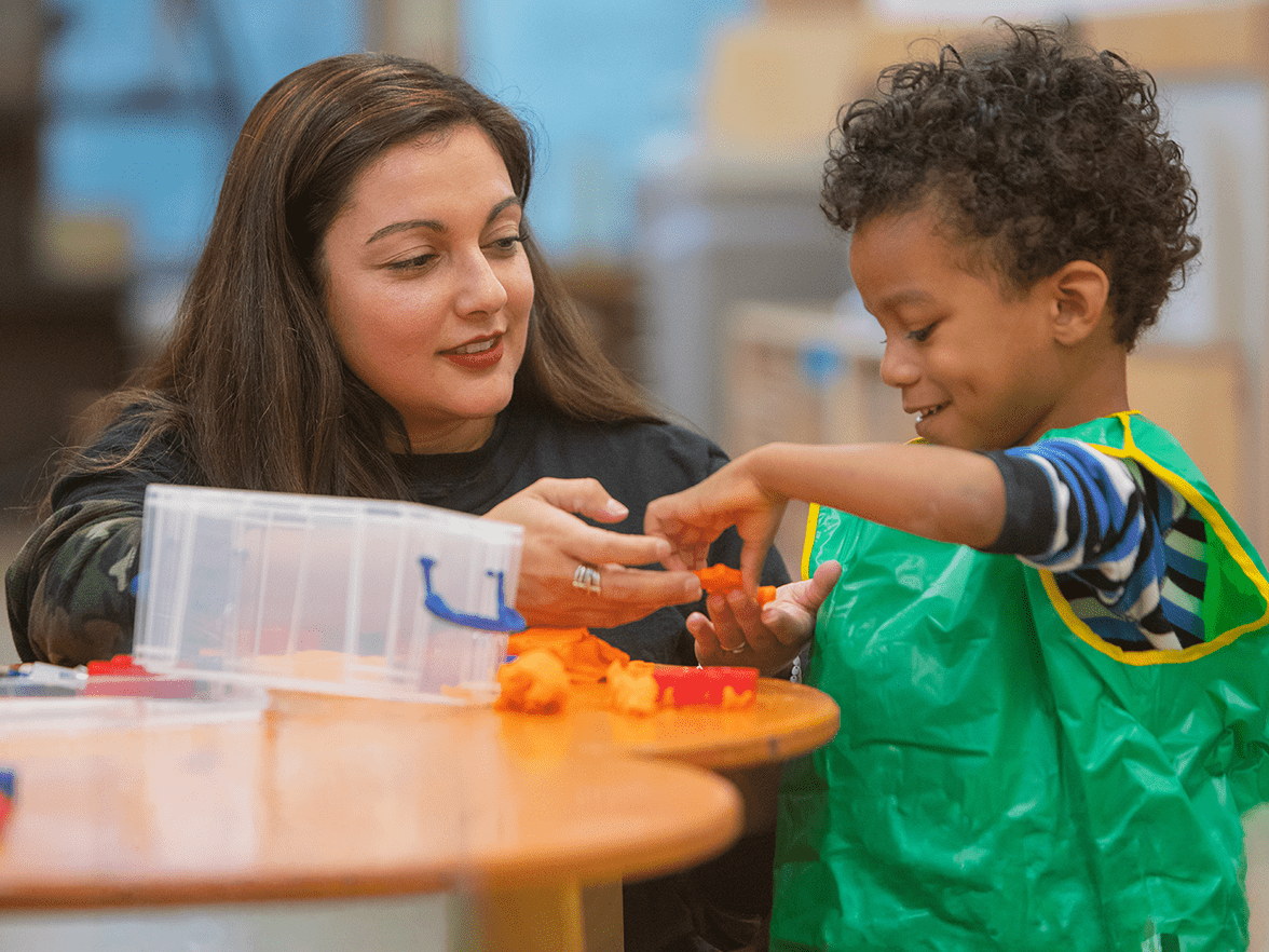 daycare teacher engaging in classroom activity with young preschooler
