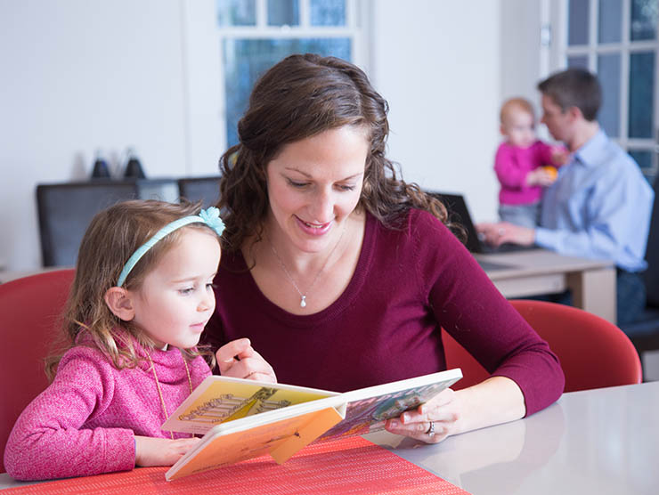 Mom reading with toddler while dad holding infant works at laptop