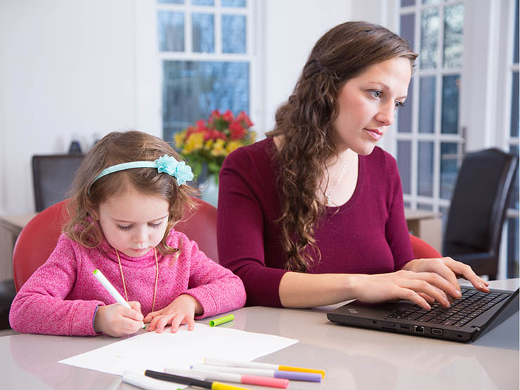 Mom on laptop next to daughter coloring