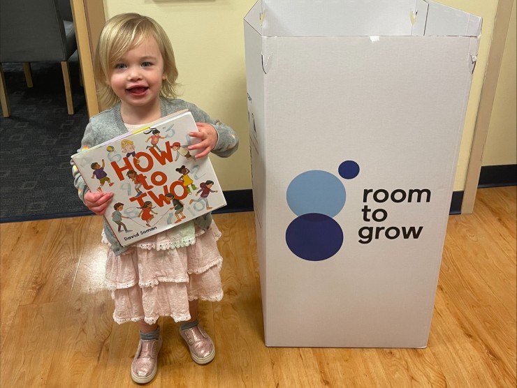 young girl holding book by donation bin 