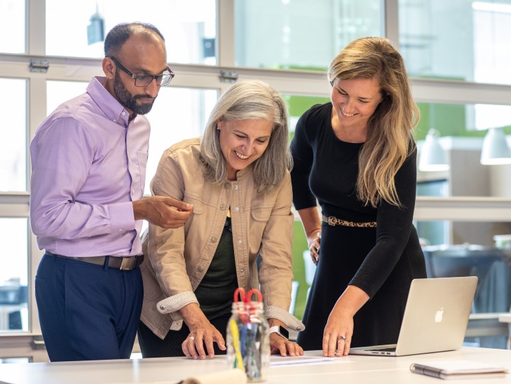 co-workers standing around table looking at laptop 