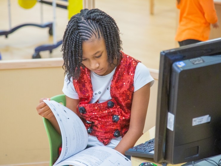 elementary student reading a book next to a computer