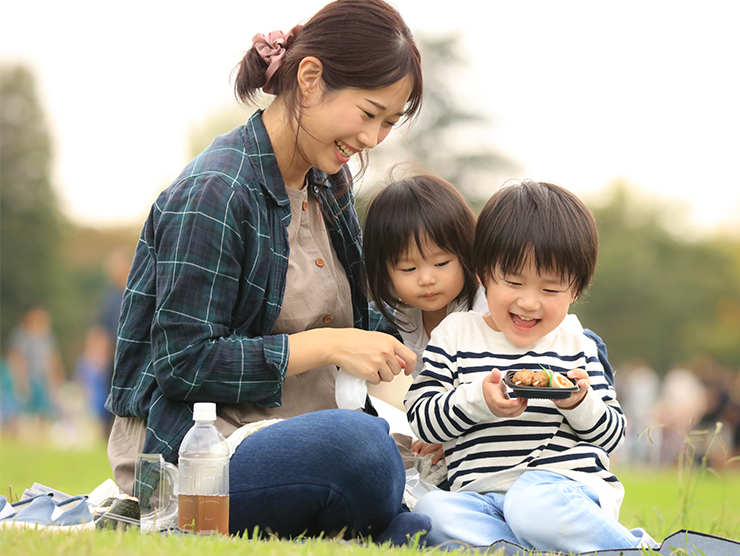 A smiling mother sits outside playing with two happy children
