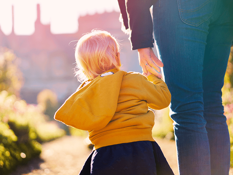 Child holding hands with an adult outdoors