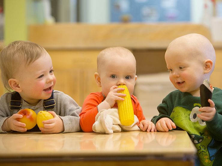 Three young toddlers in a classroom setting playing with toys.