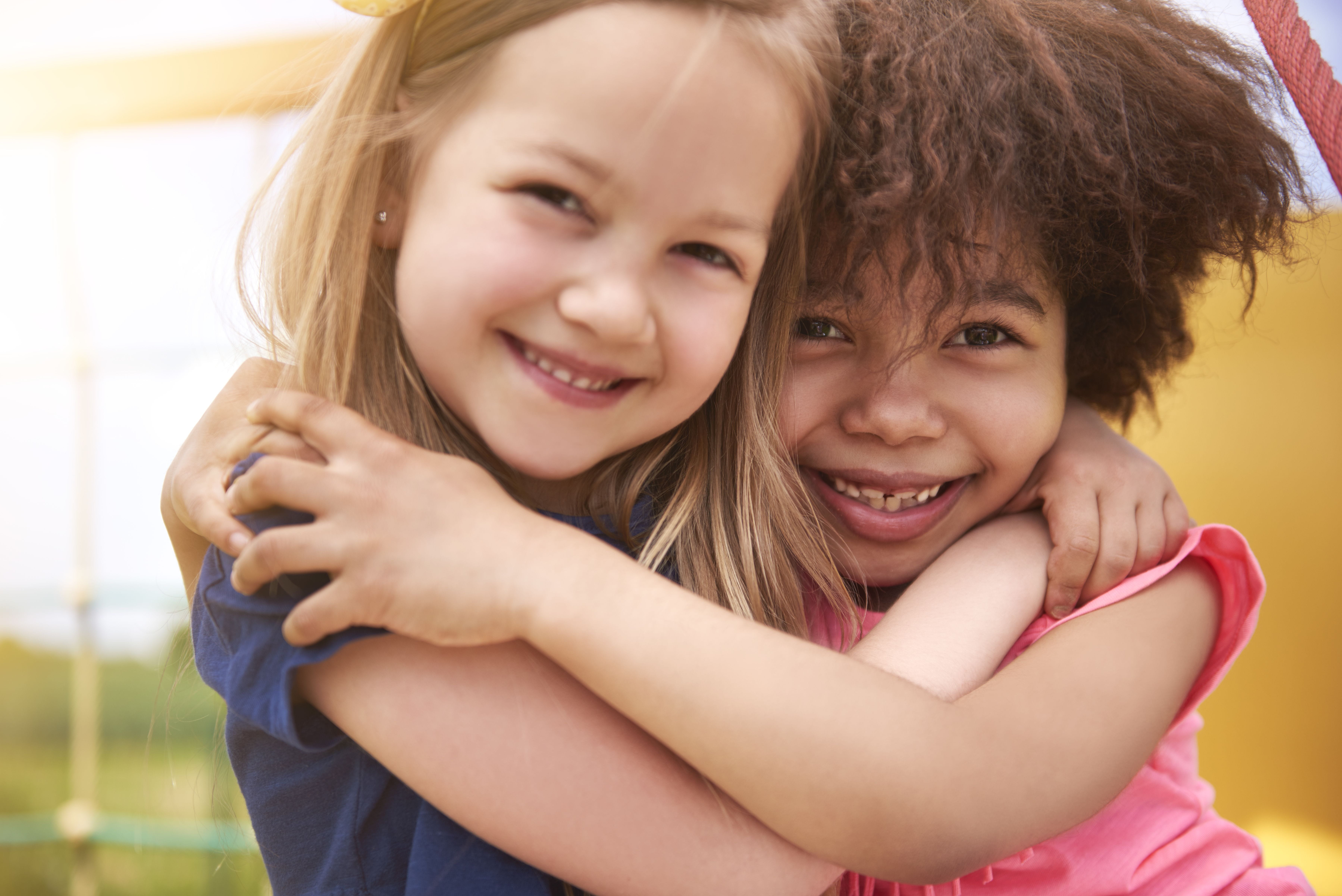 Two school-aged girls hugging and smiling at the camera