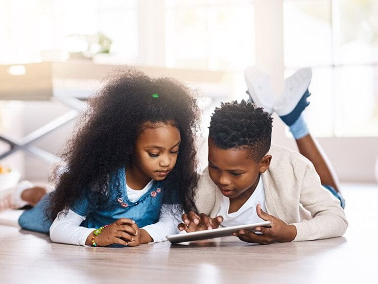 Two children playing with a tablet on the floor