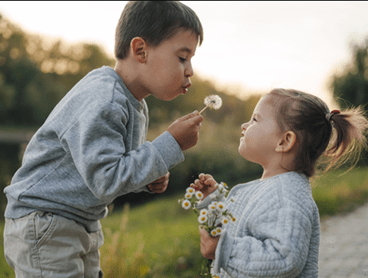 A boy blowing dandelions in his sister’s face.