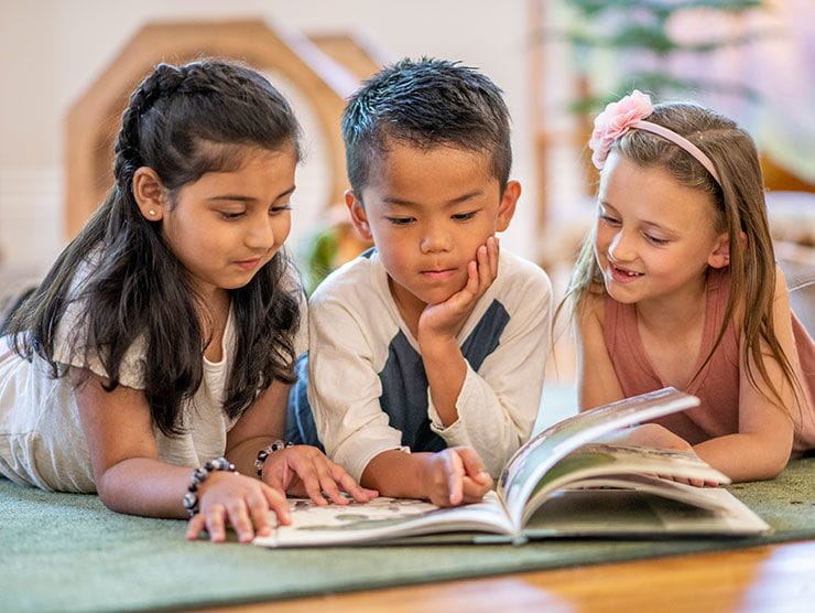 Three kindergarteners reading a book on the floor