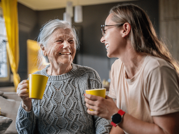 Daughter and elderly mom talking to each other while drinking out of mugs.