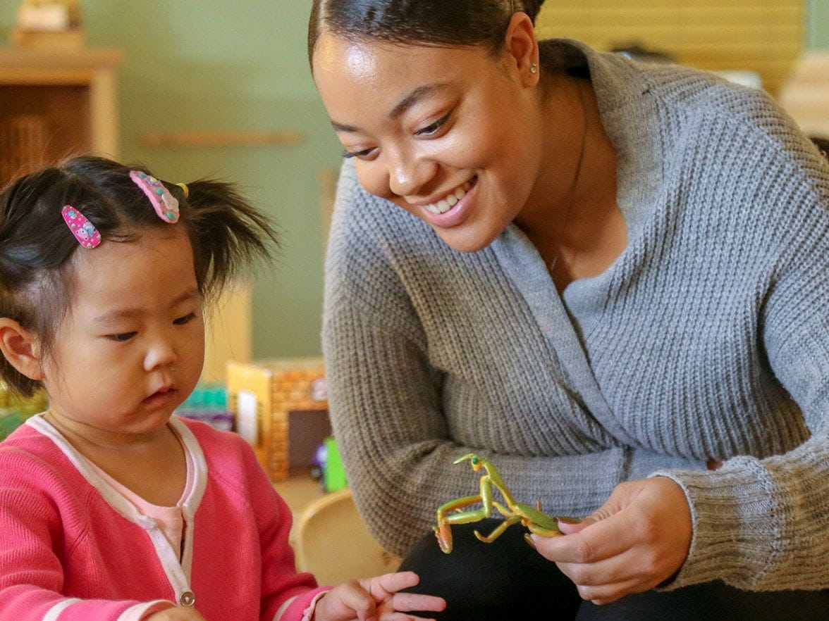A teacher in a daycare showing a toddler a toy