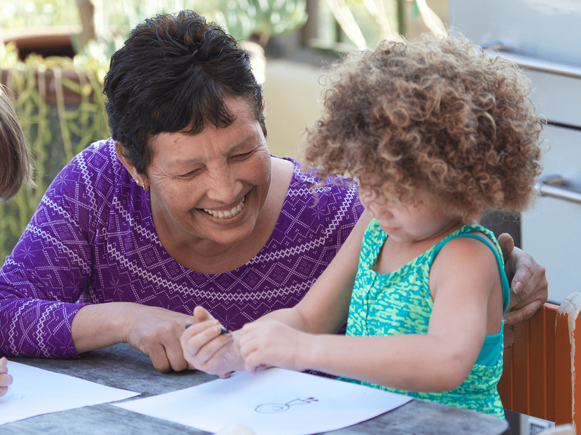A smiling woman drawing pictures with children. 