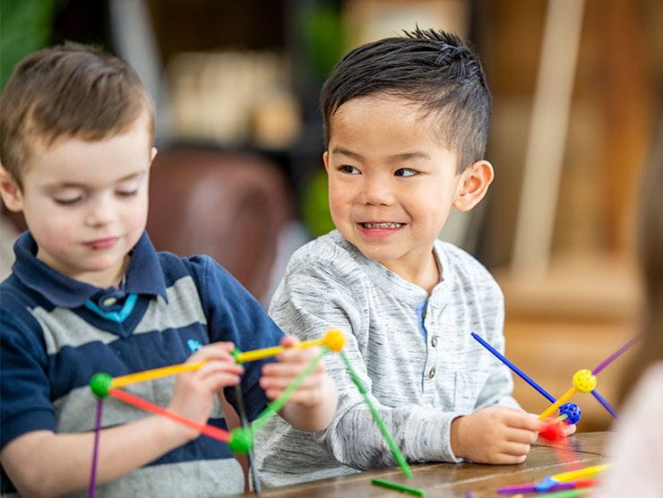 Children engaged in hands-on STEM learning, building colorful geometric structures with educational construction toys at a table.