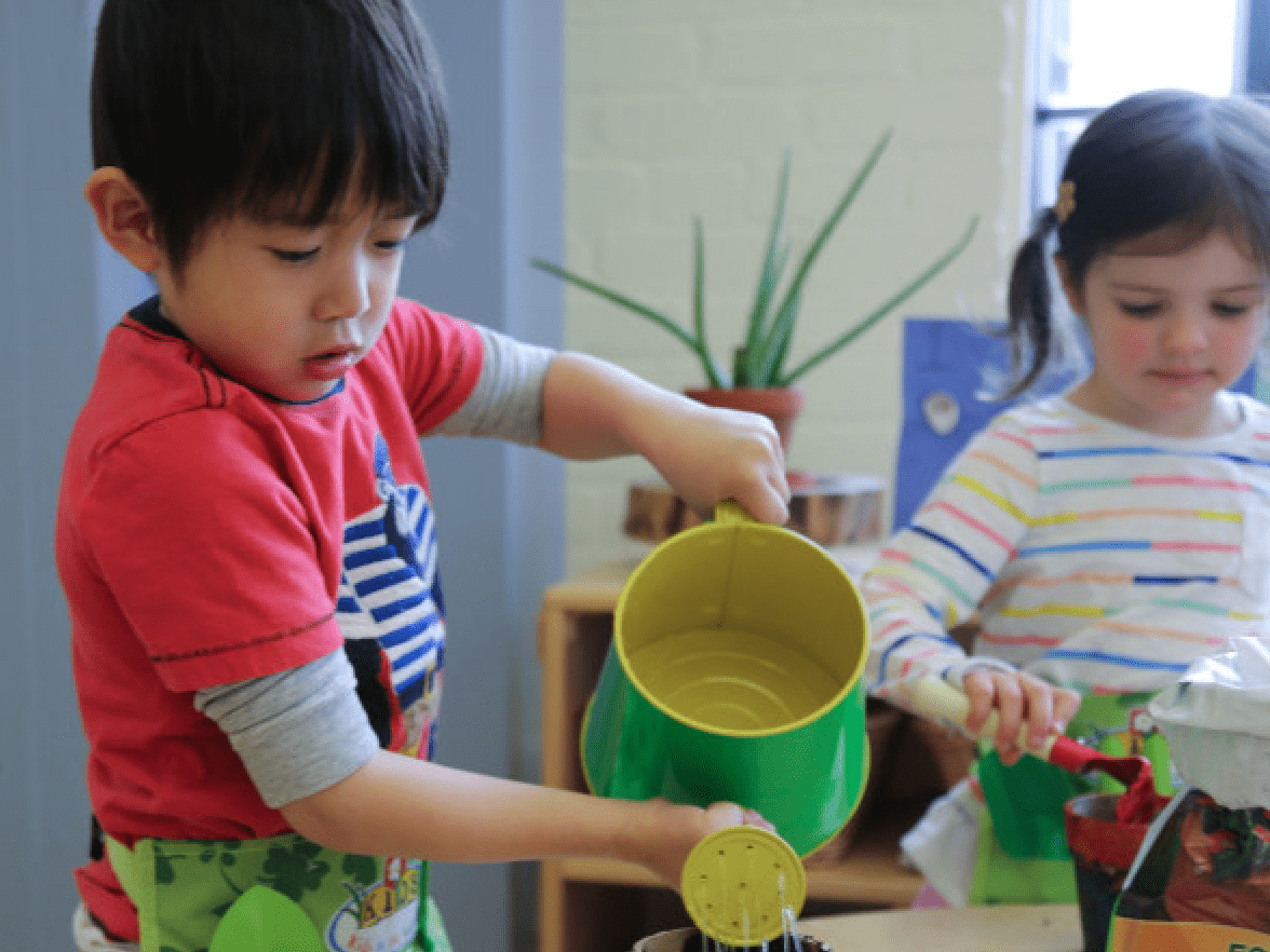 Two children watering plants in a classroom. 