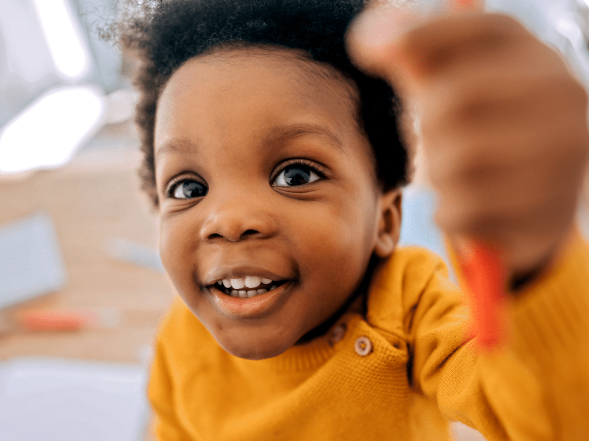 Smiling 2-3 year old toddler in toddler daycare classroom holding marker for art activity 