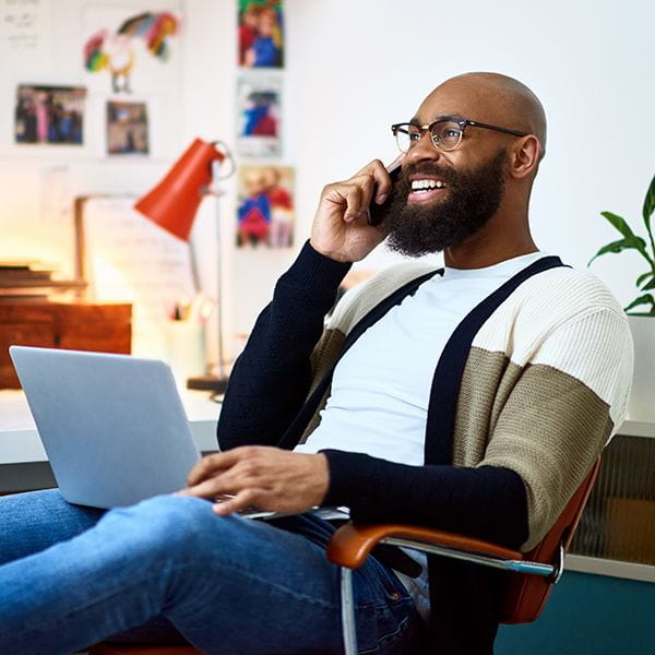 A man sitting, on the phone with a laptop