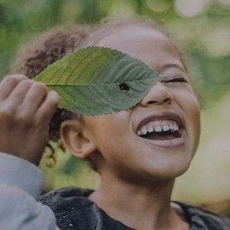 Child holding leaf over one eye outdoors in nature. 
